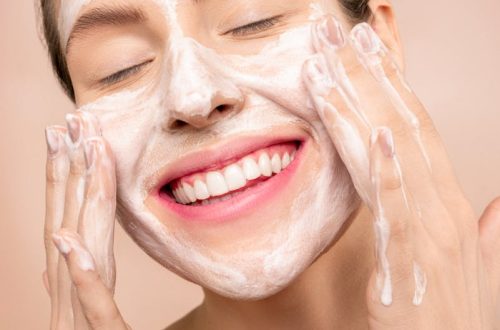 Smiling woman applies facial wash while enjoying her skincare routine, promoting happiness and skin health.