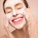 Smiling woman applies facial wash while enjoying her skincare routine, promoting happiness and skin health.